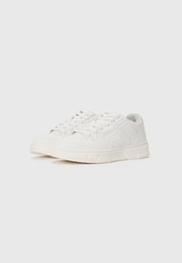 Baltas sneakers ar gludu ādas virsu, auklām, perforētiem detaļām, mīkstu apkakli un strukturētu gumijas zoli.