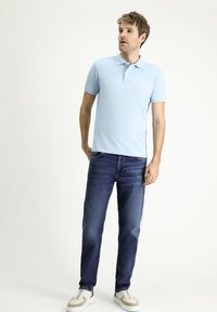 Camisa polo de color azul claro con mangas cortas, combinada con jeans azul oscuro y zapatillas blancas. Diseño simple, corte estándar y textura suave.