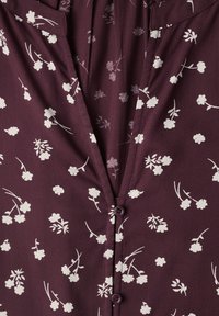 Gros plan d’un tissu couleur prune avec un motif floral blanc et deux petits boutons assortis au centre.