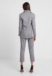 Harmaa ruudullinen puku, johon kuuluu muotitettu bleiseri ja slim-fit-housut, joissa on hienovarainen ruutukuvio ja kiiltävät mustat korkokengät.