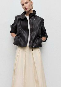 Black leather jacket with a high collar, zip front, and two front pockets, paired with a cream pleated skirt. Smooth texture, structured design.