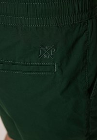 Shorts verts en tissu léger, dotés d'une taille élastique, d'une poche arrière et de détails brodés au niveau du logo.