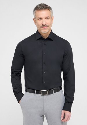 Schwarzes langärmeliges Hemd mit Knopfleiste und strukturiertem Kragen. Tragen mit hellgrauen Hosen und einem schwarzen Gürtel, der eine glatte Textur aufweist.