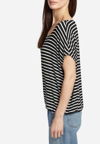Top de rayas blanco y negro de manga corta con un corte relajado, que presenta un escote ancho y una textura suave similar al algodón. Combinado con jeans de mezclilla azul.