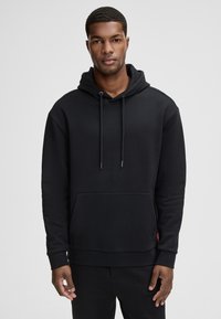 Felpa nera con cappuccio, dettagli con cordoncino, tasca kangaroo frontale, polsini e orlo a coste. Tessuto liscio con un design semplice.