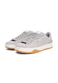 Gray suede sneakers with a rubber gum sole, padded tongue, and textured laces. Features branding on the side and a minimalistic design.