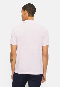 Lichtroze polo met korte mouwen, voorzien van een zachte textuur, kraag en gedetailleerde achternaad, weergegeven op een model van achteren.