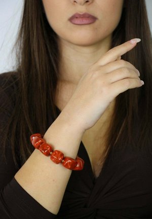 Bracciale elastico rosso con perline di resina lucida di varie forme, indossato su un polso. Lo sfondo è neutro, mettendo a fuoco l'accessorio.