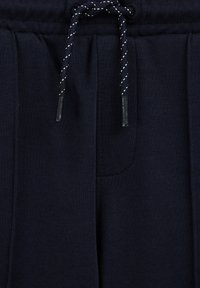 Mörkblå sweatpants med ribbad textur, elastisk midja och vit dragsko. Framlommens detaljer synliga i övre vänstra hörnet.