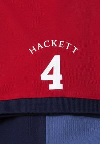 Rode stof met de tekst "HACKETT" en het nummer "4" in het wit. Het ontwerp heeft een ribbelige marineblauwe ondersectie en gladde blauwe accenten.