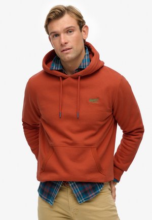 En rustfarvet hoodie med kængurulomme, snøre i hætten og broderet logo; lagdelt over en blå og grønternet skjorte.