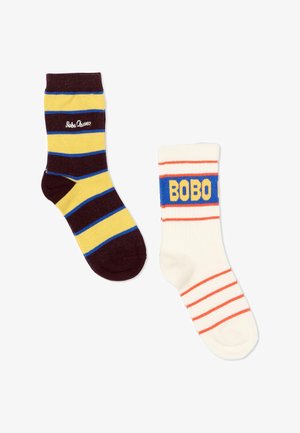Une chaussette rayée jaune et brun foncé avec le texte "Bobo Choses" ; une chaussette blanche avec des rayures orange et une bande bleue portant l'inscription "BOBO".