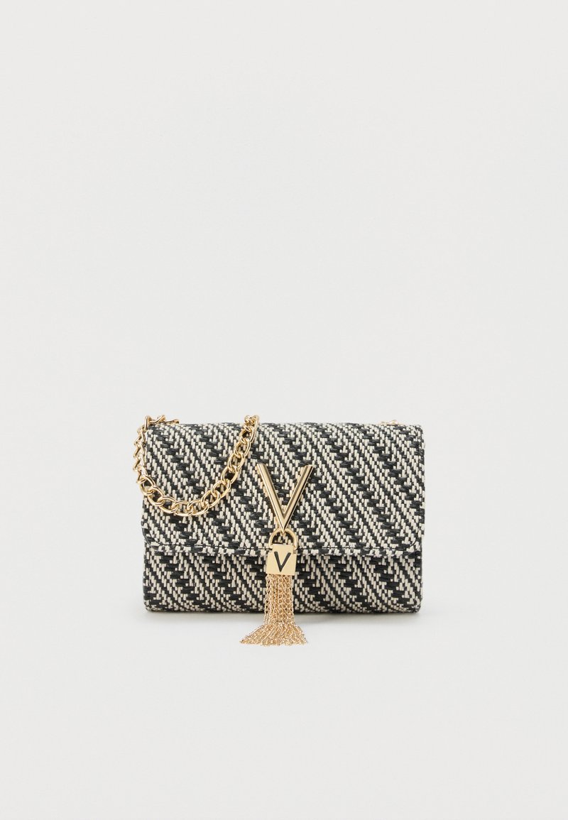 Μαύρο και άσπρο υφαντό τσαντάκι χειρός με χρυσή αλυσίδα, χρυσό κούμπωμα σε σχήμα V και λεπτομέρεια με φούντα σε απλό φόντο.