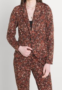 Blazer och byxset i en texturerad, flerfärgad djurmönstring. Predominant i orange och svart med vita accenter, med en knappstängning.