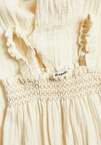 Lichtcrème muslin jurk met ruches op de schouderbanden en een smock-borstel. Heeft een zachte textuur en subtiele plooien voor een vloeiende uitstraling.