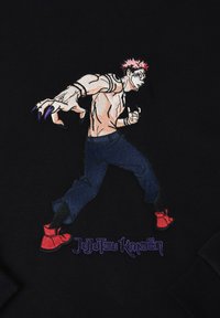Sweat-shirt noir arborant un personnage brodé avec des cheveux roses, une carrure musclée, un jean bleu et des chaussures rouges. Le texte indique "Jujutsu Kaisen" en violet.