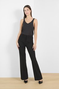 Débardeur noir à col en V associé à un pantalon noir à taille haute et évasé, ainsi qu'à des chaussures noires pointues, le tout sur fond minimaliste.