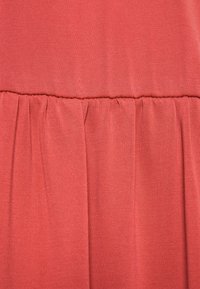 Röd vävd tyg med en rynkad design vid midjan och vertikala veck, vilket skapar textur och dimension. Slät finish över hela ytan.