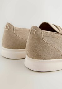 Chaussures beige en daim à enfiler avec semelles en caoutchouc blanc vues de dos sur un fond clair.