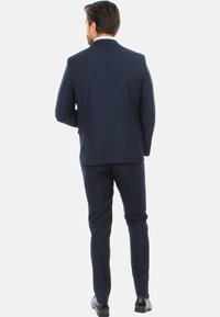 Abito blu navy con vestibilità su misura, spacchetto singolo sul retro, texture sottile, abbinato a scarpe lucide, visto dal retro.