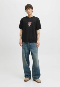 Sort bomulds t-shirt med et grafik af et trofæ i rødt, parret med løse blå denim jeans og beige slips-on sko.