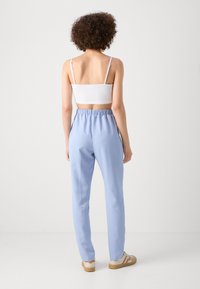 Lyseblå bukser med strikk i livet, kombinert med en hvit kort topp. Glatt tekstur, subtilt design, og tettsittende silhuett.