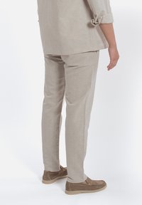 Pantaloni in lino beige con taglio dritto e risvolti, abbinati a scarpe in suede marrone chiaro con suola in gomma.