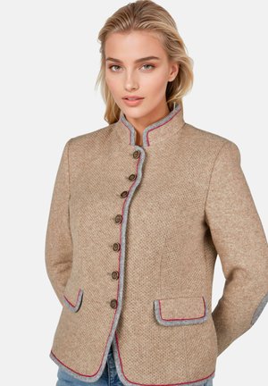 Vrouw met blond haar die een beige textuurjasje draagt met grijze en rode biezen, bruine knopen en voorzakken met kleppen tegen een witte achtergrond.
