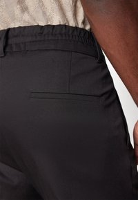 Czarne, dopasowane spodnie o gładkiej teksturze, z elastycznym pasem i tylnią kieszenią. Zbliżenie na tkaninę i dopasowanie.