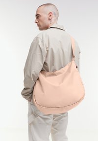 Borsa a spalla color pescato realizzata in morbido tessuto, con una forma grande e rotonda e una singola tracolla regolabile. Branding sottile visibile.