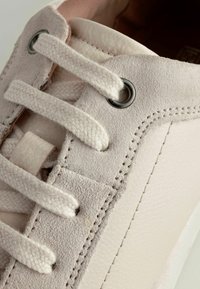 Hellrosa Wildleder-Sneaker mit Baumwollschnürsenkeln, metallischen Ösen und kontrastierenden Nähten. Besitzt eine glatte Textur und eine abgerundete Form.