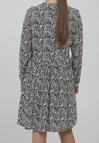 Musta-valkoisella kuviolla varustettu mekko pitkähihaisilla, vartalonmyötäisellä vyötäröllä ja levenevällä hameella. Tekstuuri näyttää sileältä ja kevyeltä.