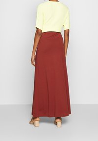 Lys gul tekstureret crop top parret med en lang rustfarvet nederdel. Outfittet har en tætsiddende talje og et flydende design. Sandaler med blokhæl.