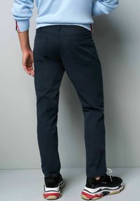 Marineblauwe broek met een slim fit, achterzakken en een subtiele textuur, gecombineerd met zwarte sneakers met multiculturele accenten.