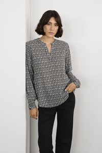 Blusa a maniche lunghe in bianco e nero con un motivo geometrico a foglie, design senza colletto e vestibilità rilassata, abbinata a pantaloni neri.