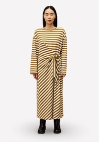 Gestreepte langarm jurk in bruin en crème, met een gedraaide knoopdetail in de taille. Draag het met zwarte enkellaarsjes.