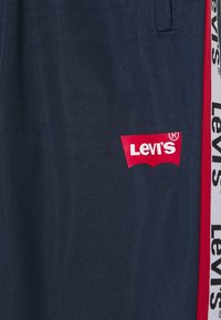 Marineblaue Sporthosen aus strukturiertem Stoff, mit einem auffälligen roten Levi's-Logo und einem weißen Markenstreifen an der Seite.