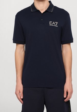 Polo shirt blu navy con maniche corte, colletto con cucitura bianca e logo EA7 Emporio Armani sul lato sinistro del petto.