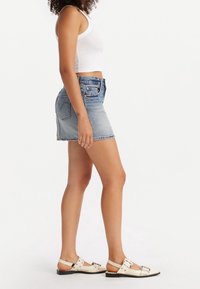 Lichtblauwe denim minirok met vervaagde textuur, gecombineerd met een witte geribbelde tanktop en crème kleurige sandalen met een gesp detail.