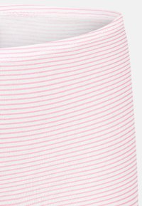 Närbild av mjukt tyg med tunna horisontella rosa ränder på en vit bakgrund, som visar en böjd söm eller kant.