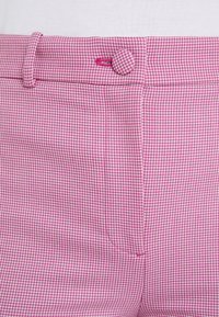 Roze geruite broek met een knoopsluiting, riemlussen en een textuurstof, voorzien van een opvallend klein ruitpatroon door het hele stuk.
