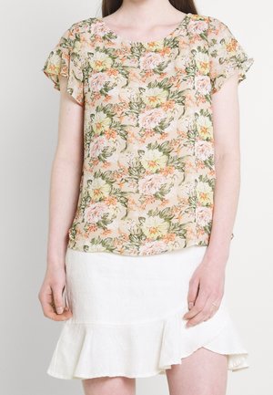 Nainen, jolla on lyhythihainen kukkakuosinen pusero, jossa persikan, keltaisen ja vihreän sävyt, yhdistettynä valkoiseen röyhelöiseen hameeseen.