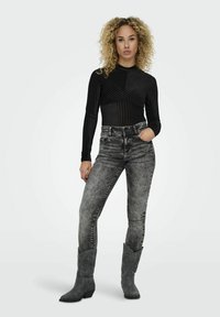 Top nero a maniche lunghe con texture a righe verticali, abbinato a jeans grigi sbiaditi e stivali da cowboy grigi impreziositi.