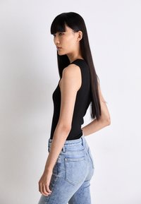 Svart ärmlös topp med ribbad textur, kombinerad med ljusblå högmidjade jeans med klassisk fem-ficksdesign.