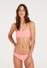 Ružový bikiny set s ribbed štruktúrou, obsahujúci skrátený top s nastaviteľnými ramienkami a zodpovedajúce nízko-risovité spodky, obidva s vlnitými okrajmi.