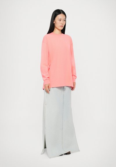 Pink long-sleeve shirt with a round neckline, paired with a light blue denim maxi skirt featuring a side slit and visible stitching details.
