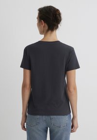 Gray cotton t-shirt with short sleeves, crew neck, and a relaxed fit. Worn with blue denim jeans, showcasing a simple, casual design.