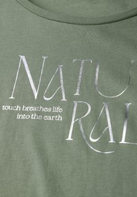 Zelené bavlněné tričko s stříbrným nápisem "NATURAL" a pod ním bílým textem "dotek dává život Zemi".