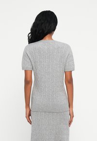 Maglione corto a maniche corte grigio chiaro in maglia, con un motivo a treccia strutturato, caratterizzato da una vestibilità rilassata e orlo a coste. La vista posteriore mostra una finitura liscia.