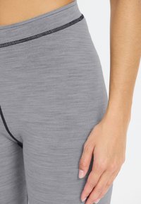 Grå atletiske leggings med en glat tekstur, med en sort syet talje og et tætsiddende design. Hånd hviler nærliggende.